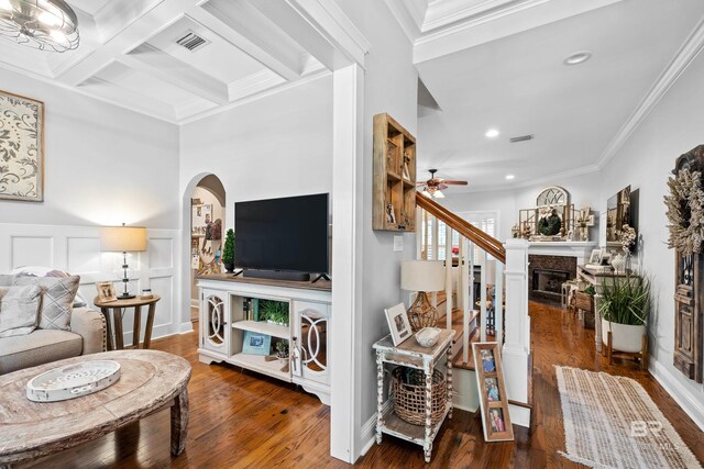 living area with crown molding, beam ceiling, hardwood / wood-style floors, a ceiling fan, and visible vents