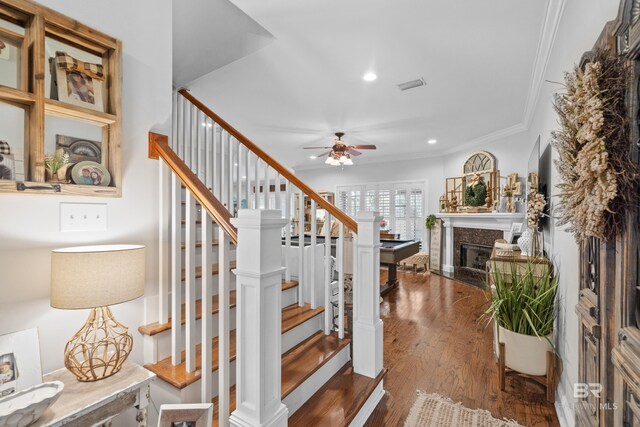 stairway with a ceiling fan, crown molding, a high end fireplace, wood finished floors, and recessed lighting