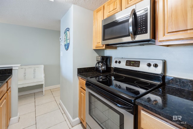 23044 Perdido Beach Blvd Unit 338, Orange Beach, AL 36561 - kitchen with stainless steel appliances, baseboards, light tile patterned flooring, dark stone counters, and a textured ceiling