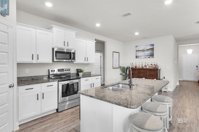 9365 Eiland Dr, Foley, AL 36535 - kitchen with stainless steel appliances, a sink, light wood finished floors, white cabinets, and dark stone countertops
