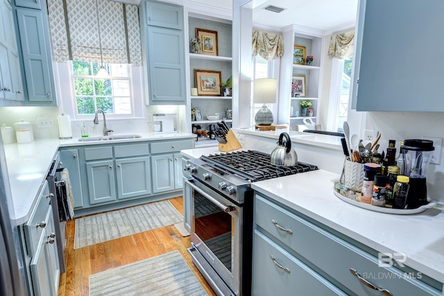 kitchen with light hardwood / wood-style floors, ornamental molding, high end stove, sink, and blue cabinets