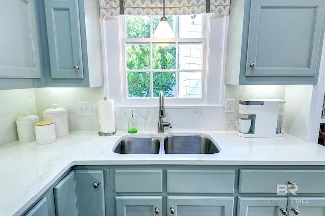 kitchen with sink, tasteful backsplash, light stone counters, and decorative light fixtures