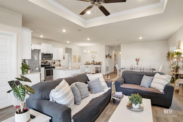 living room with a tray ceiling, ceiling fan, and light wood-type flooring