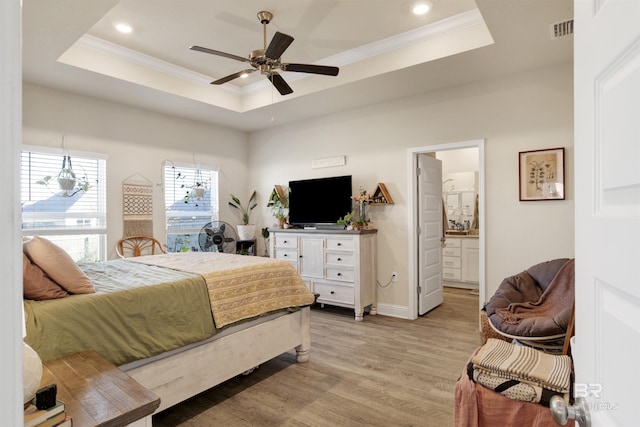 bedroom with connected bathroom, light hardwood / wood-style flooring, a raised ceiling, and ceiling fan