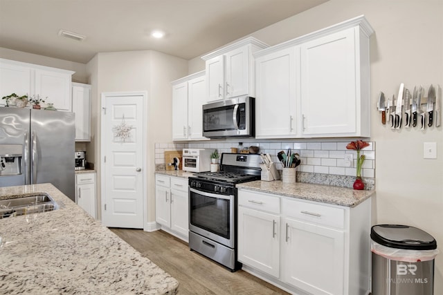 kitchen with white cabinets, appliances with stainless steel finishes, backsplash, and light wood-type flooring