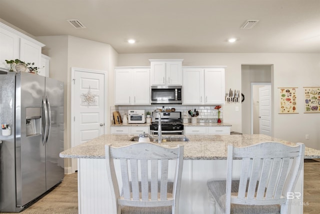 kitchen with white cabinets, decorative backsplash, stainless steel appliances, and a kitchen island with sink