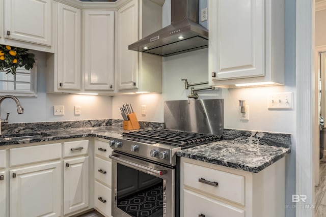 kitchen with white cabinets, wall chimney exhaust hood, high end stove, and sink