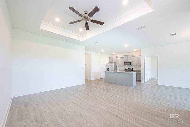 394 Haise Ln, Gulf Shores, AL 36542 - unfurnished living room featuring a tray ceiling, baseboards, light wood finished floors, recessed lighting, and crown molding