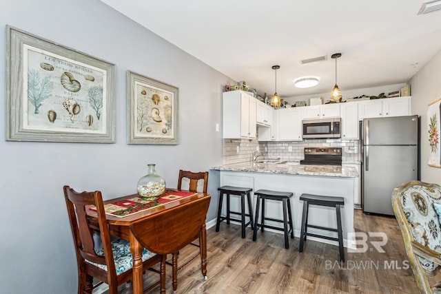 kitchen featuring backsplash, pendant lighting, kitchen peninsula, white cabinetry, and appliances with stainless steel finishes