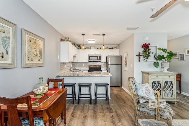 kitchen with white cabinetry, kitchen peninsula, stainless steel appliances, tasteful backsplash, and light stone countertops