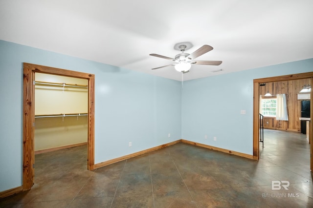 unfurnished bedroom featuring a ceiling fan, visible vents, baseboards, dark tile patterned flooring, and a walk in closet