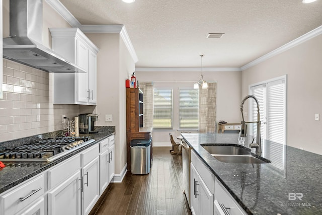 kitchen featuring visible vents, ornamental molding, wall chimney exhaust hood, a sink, and stainless steel appliances