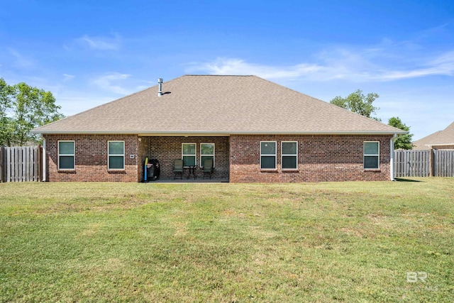 rear view of property with a lawn, brick siding, a fenced backyard, and roof with shingles