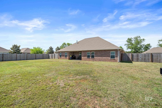 back of property featuring a fenced backyard, a yard, and brick siding