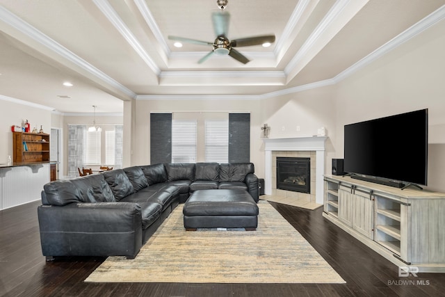 living room with a ceiling fan, a tiled fireplace, ornamental molding, and a raised ceiling