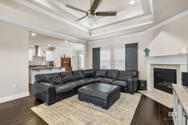 living area with a ceiling fan, a fireplace, hardwood / wood-style flooring, ornamental molding, and a tray ceiling