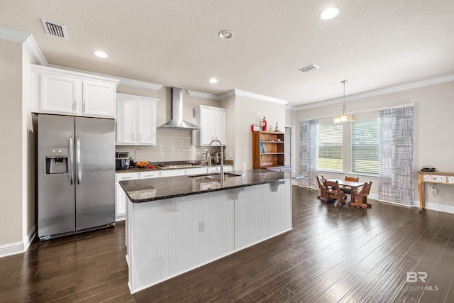 kitchen with visible vents, an island with sink, wall chimney range hood, white cabinetry, and stainless steel appliances