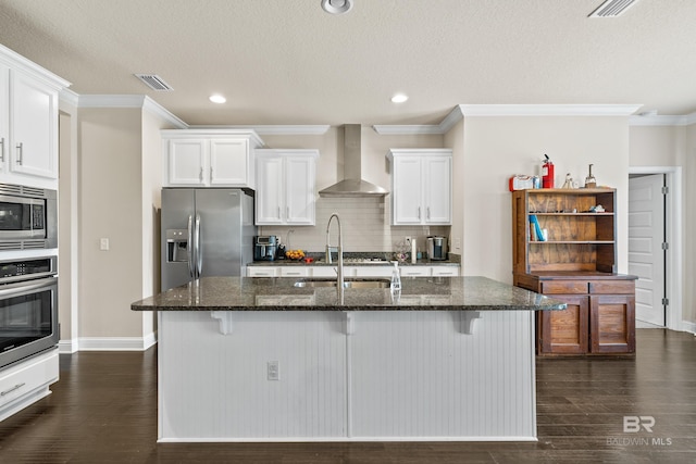 kitchen featuring visible vents, ornamental molding, wall chimney range hood, dark stone counters, and appliances with stainless steel finishes