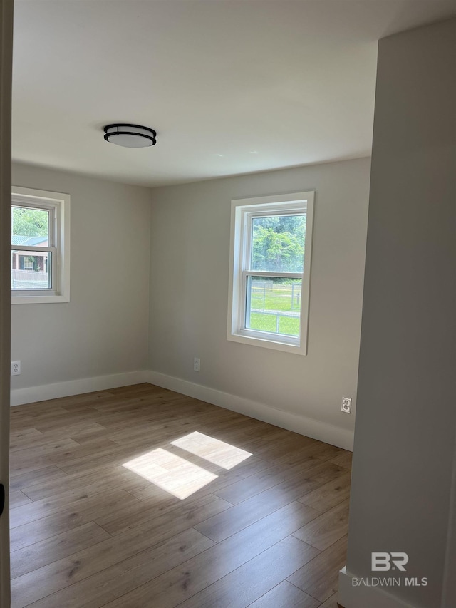 empty room with a wealth of natural light, baseboards, and wood finished floors