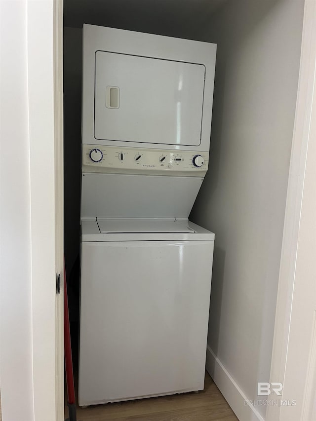 laundry area featuring baseboards, laundry area, light wood-style flooring, and stacked washer / drying machine
