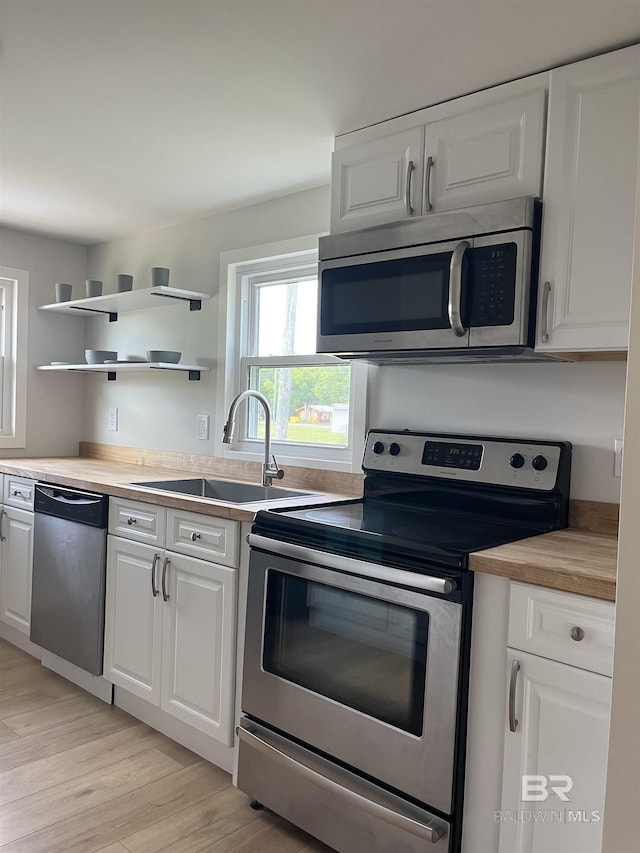 kitchen featuring a sink, stainless steel appliances, light wood-style flooring, white cabinetry, and light countertops