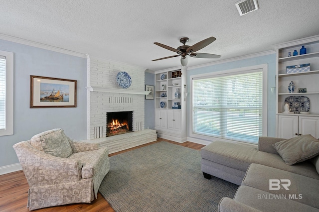 living room with ceiling fan, hardwood / wood-style flooring, a brick fireplace, and a textured ceiling