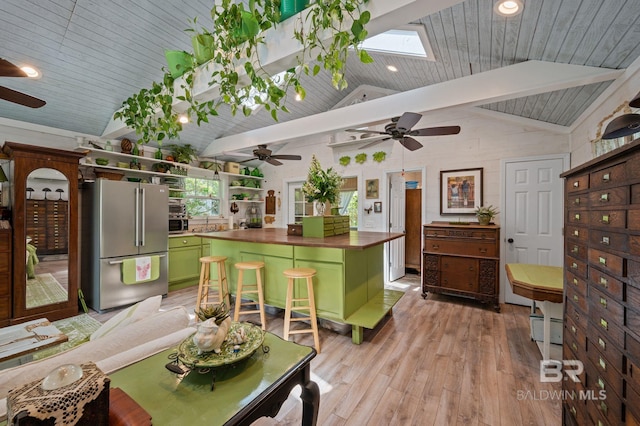 kitchen with vaulted ceiling with skylight, wood ceiling, green cabinetry, light hardwood / wood-style flooring, and stainless steel refrigerator