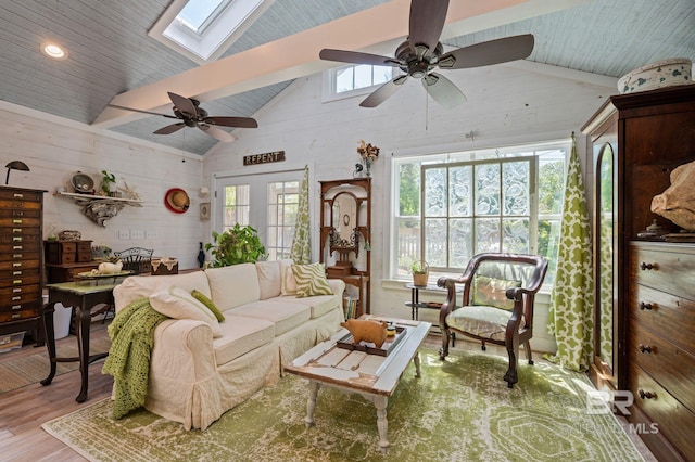 living room with ceiling fan, a skylight, light wood-type flooring, and beam ceiling