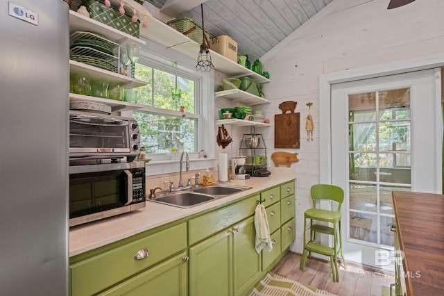 kitchen featuring light hardwood / wood-style floors, wood walls, sink, appliances with stainless steel finishes, and vaulted ceiling