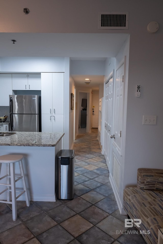 kitchen featuring a breakfast bar area, light stone counters, stainless steel refrigerator, and white cabinets