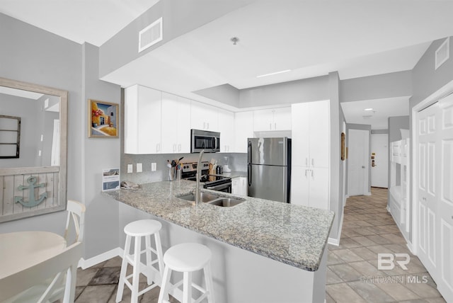 kitchen with white cabinets, light stone counters, stainless steel appliances, kitchen peninsula, and a kitchen breakfast bar