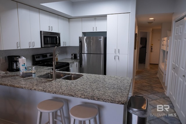 kitchen with white cabinets, appliances with stainless steel finishes, light stone countertops, kitchen peninsula, and a breakfast bar area