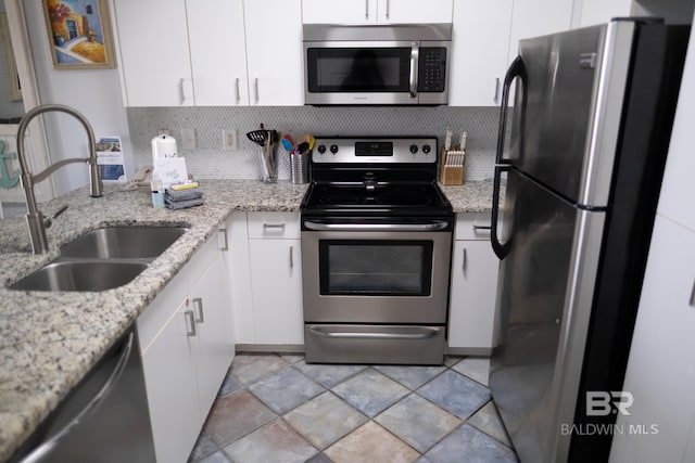 kitchen with light stone counters, stainless steel appliances, white cabinetry, and sink