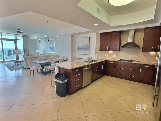 kitchen featuring a sink, a tray ceiling, dishwasher, and wall chimney exhaust hood