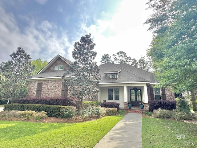 craftsman-style home with a front yard, french doors, brick siding, and roof with shingles
