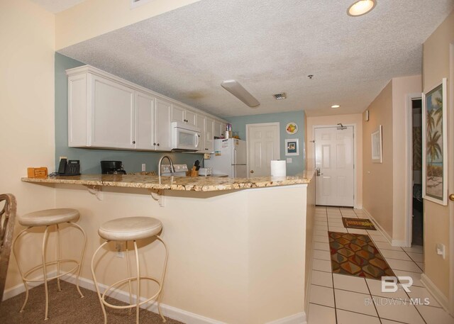 527 Beach Club Trl Unit C1006, Gulf Shores, AL 36542 - kitchen with white appliances, light stone counters, light tile patterned floors, white cabinetry, and a peninsula