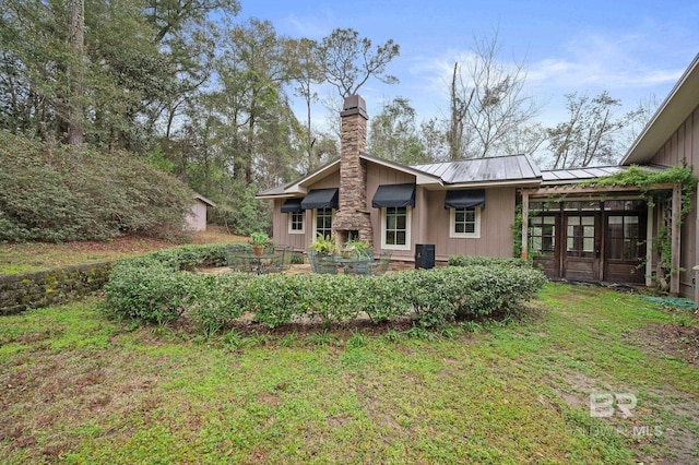 back of property with metal roof, a yard, a chimney, and a standing seam roof