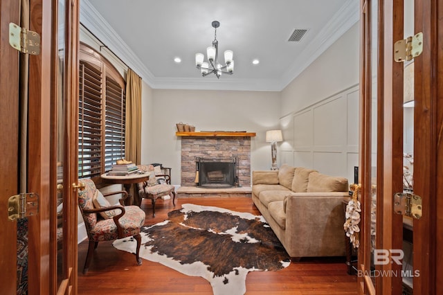 living room featuring wood finished floors, visible vents, a stone fireplace, crown molding, and a decorative wall