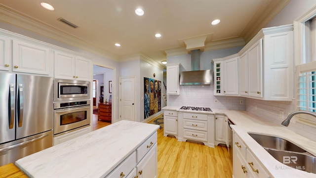 kitchen with white cabinetry, appliances with stainless steel finishes, light hardwood / wood-style flooring, crown molding, and wall chimney range hood