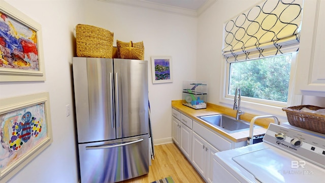 kitchen with sink, washer / dryer, white cabinets, stainless steel fridge, and light wood-type flooring