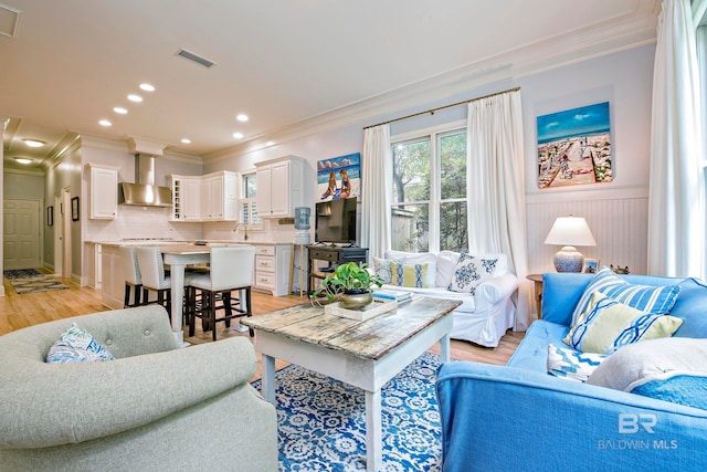 living room with light hardwood / wood-style floors, sink, and ornamental molding