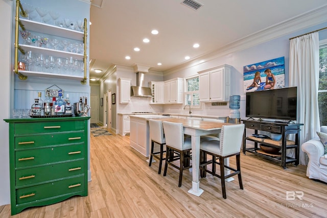 kitchen featuring a center island, wall chimney exhaust hood, a healthy amount of sunlight, and white cabinets