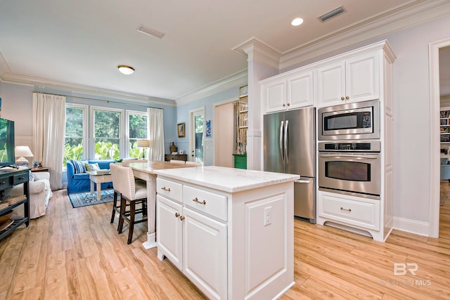 kitchen with appliances with stainless steel finishes, crown molding, a kitchen island, white cabinets, and light wood-type flooring