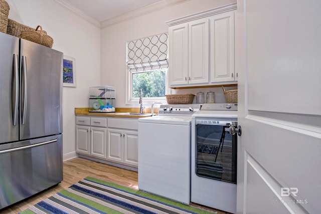 clothes washing area featuring cabinets, sink, ornamental molding, light wood-type flooring, and washing machine and dryer