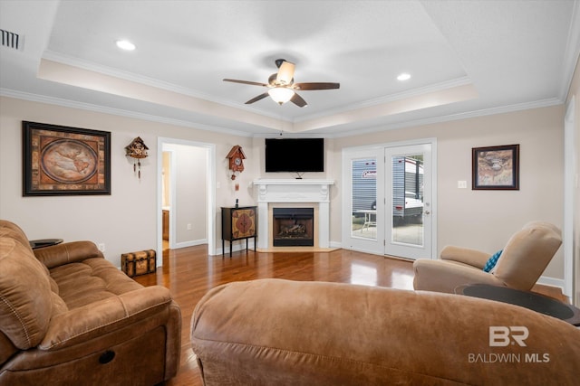 living room with crown molding, ceiling fan, wood-type flooring, and a tray ceiling