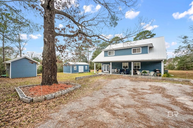 view of front of house featuring a porch, metal roof, an outdoor structure, and dirt driveway