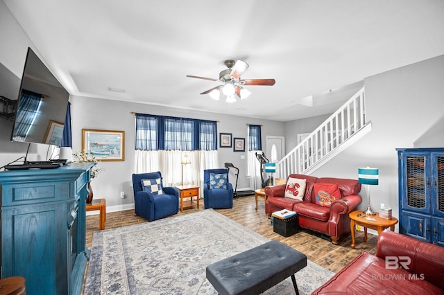 living room with a ceiling fan, baseboards, stairway, and wood finished floors