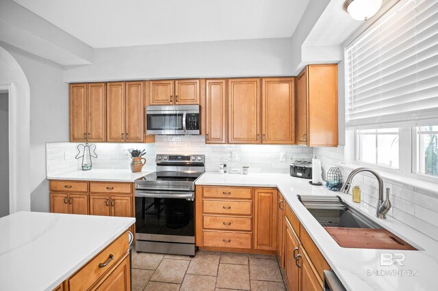 kitchen featuring brown cabinets, stainless steel appliances, light countertops, decorative backsplash, and a sink