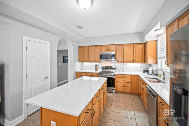 kitchen with decorative backsplash, appliances with stainless steel finishes, brown cabinetry, a sink, and a kitchen island