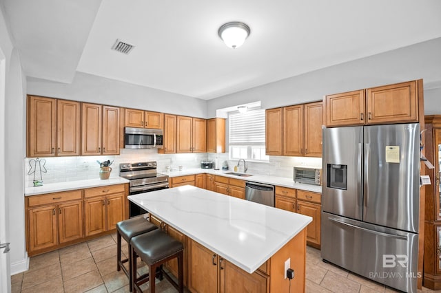 kitchen featuring stainless steel appliances, visible vents, backsplash, a sink, and a kitchen island